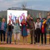The image features a group of people posing for a photo outdoors with their hands aloft. The individuals are standing on a baseball field and a cloudy sky above. Photo by kmr studios.