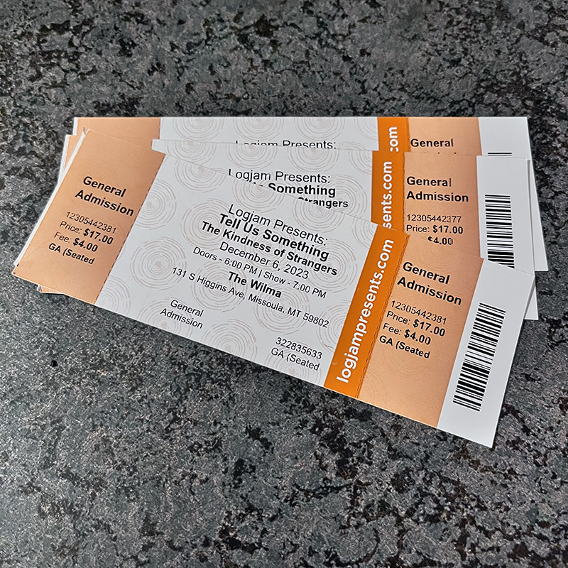 The image shows two admission tickets for Tell Us Something. The tickets are sitting on top of a table.