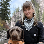 The image shows a woman posing outdoors with her dog in the mountains.