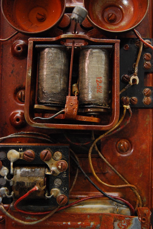 The image features a close-up of a device with a time stamp of 12:52. The setting is indoors, and the device shows signs of rust, indicating that it may be old or abandoned. It is the interior of a vintage wall phone.
